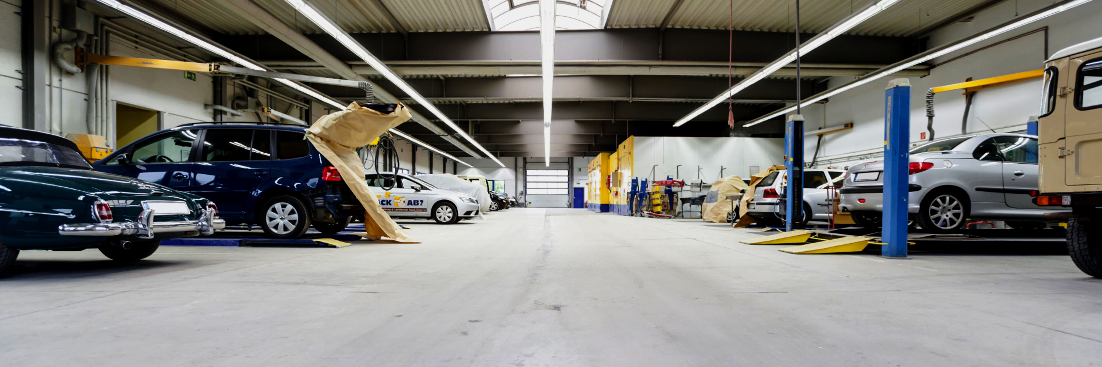 Autowerkstatt mit Fahrzeugen welche links und rechts am rand stehen. in der mitte des bildes ist ein rolltor zu sehen